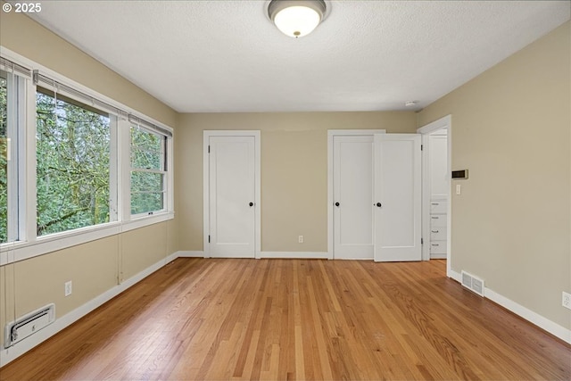 unfurnished bedroom with a textured ceiling, light wood-style flooring, visible vents, multiple closets, and baseboards