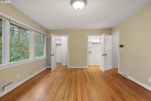 unfurnished bedroom featuring a textured ceiling, light wood finished floors, visible vents, and baseboards