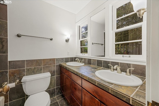 bathroom featuring a sink, tile walls, toilet, and double vanity