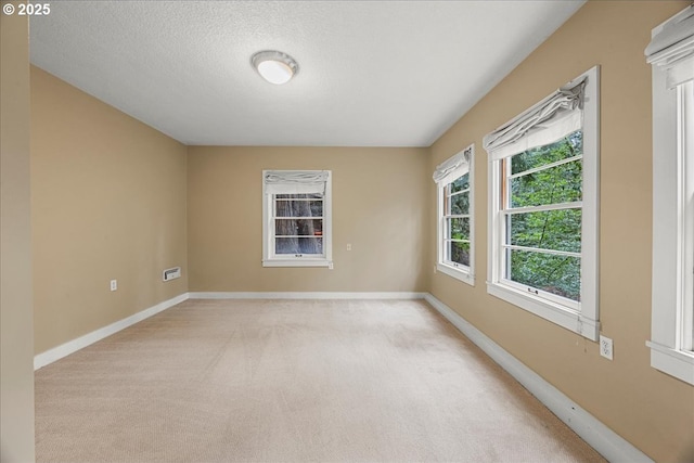 spare room featuring baseboards, a textured ceiling, and light colored carpet