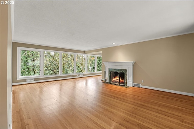 unfurnished living room with visible vents, baseboards, ornamental molding, light wood-style floors, and a high end fireplace