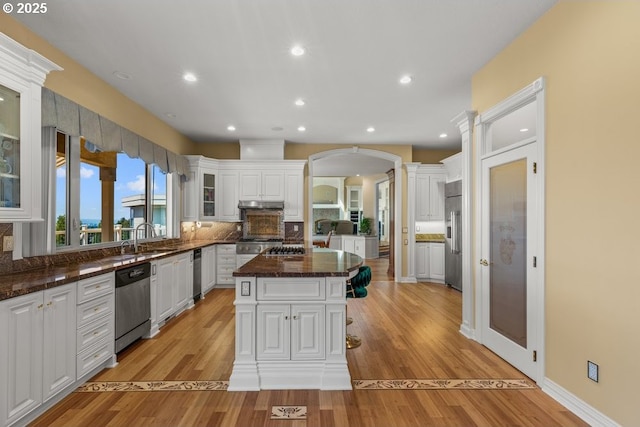 9337 SE Pennington Ct, Happy Valley, OR 97086 - kitchen with appliances with stainless steel finishes, arched walkways, a kitchen island, white cabinets, and light wood-style flooring