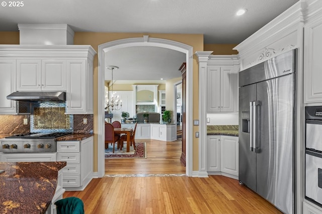 9337 SE Pennington Ct, Happy Valley, OR 97086 - kitchen featuring stainless steel appliances, under cabinet range hood, arched walkways, light wood finished floors, and white cabinetry