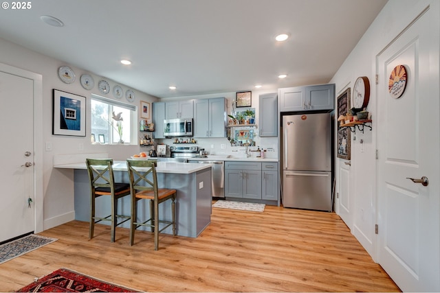 kitchen featuring appliances with stainless steel finishes, gray cabinetry, light hardwood / wood-style floors, and a breakfast bar area