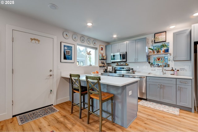 kitchen featuring sink, light hardwood / wood-style flooring, gray cabinets, a breakfast bar, and appliances with stainless steel finishes