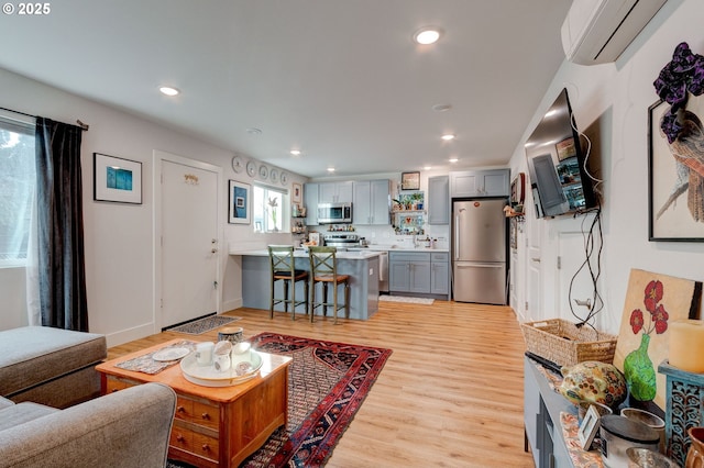 living room with sink, a wall mounted AC, light wood-type flooring, and plenty of natural light