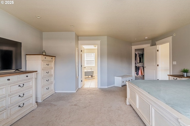 bedroom with baseboards, ensuite bath, a walk in closet, and light colored carpet