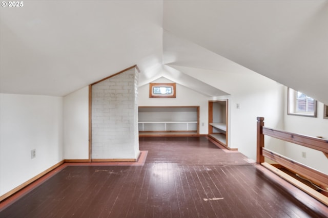 bonus room with built in shelves, dark wood-type flooring, and vaulted ceiling