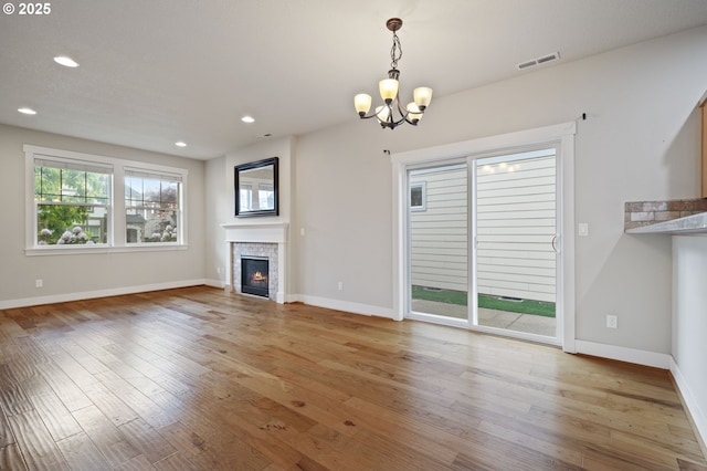 unfurnished living room with a chandelier, a fireplace, light wood-type flooring, baseboards, and recessed lighting