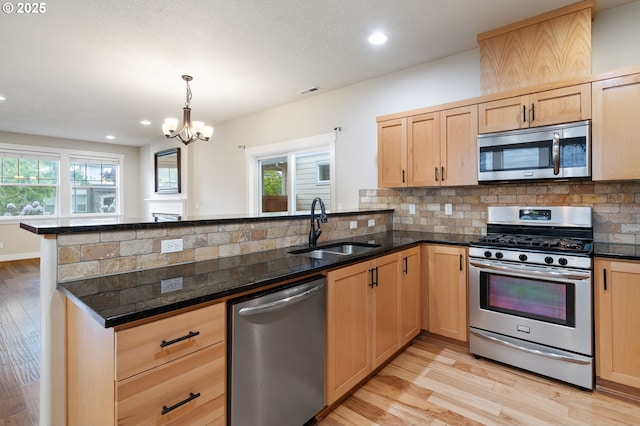 kitchen featuring appliances with stainless steel finishes, light brown cabinetry, a sink, a peninsula, and light wood-style floors