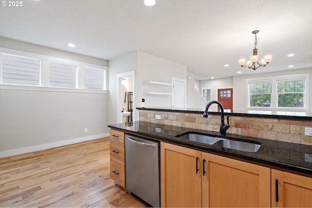 kitchen featuring stainless steel dishwasher, a sink, backsplash, light wood finished floors, and dark stone countertops