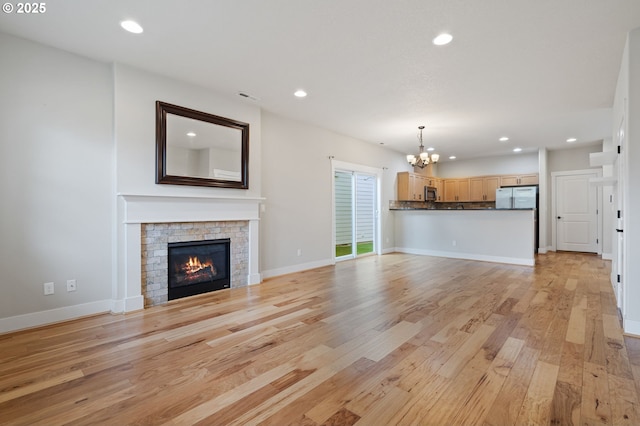 unfurnished living room featuring a chandelier, light wood finished floors, recessed lighting, a glass covered fireplace, and baseboards