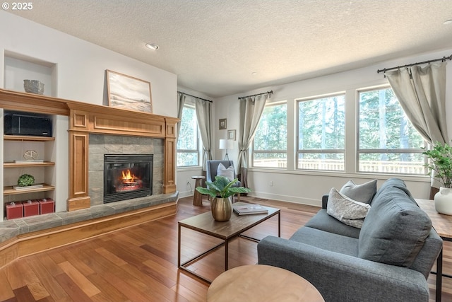 living room with a fireplace, a textured ceiling, baseboards, and wood finished floors