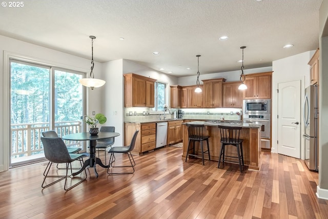 kitchen with a kitchen island, plenty of natural light, a sink, light wood-style floors, and appliances with stainless steel finishes