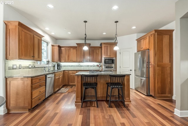 kitchen featuring a kitchen island, a sink, appliances with stainless steel finishes, a kitchen breakfast bar, and backsplash