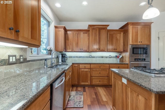 kitchen featuring a sink, backsplash, stainless steel appliances, brown cabinetry, and light wood finished floors