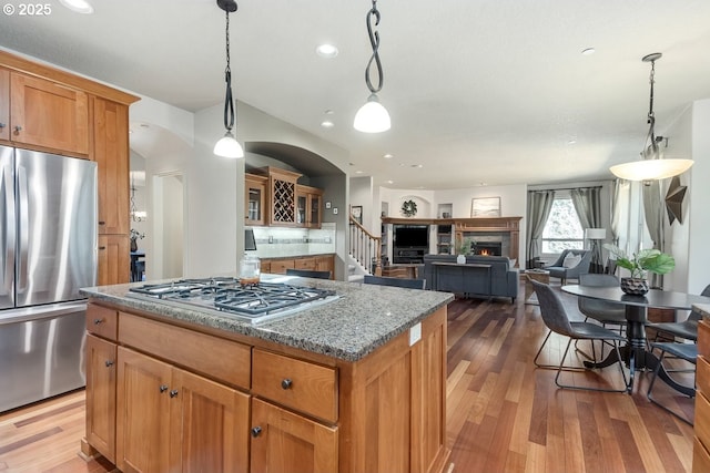 kitchen with a center island, a warm lit fireplace, stainless steel appliances, and wood finished floors