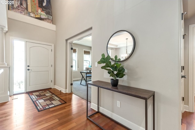 foyer entrance featuring decorative columns, baseboards, and wood finished floors