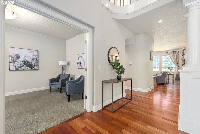 hall with decorative columns, wood finished floors, baseboards, and a textured ceiling