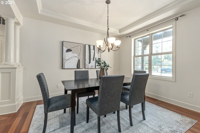 dining room with wood finished floors, a raised ceiling, baseboards, and decorative columns