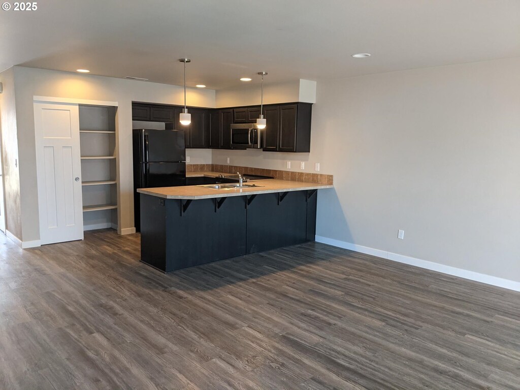 kitchen with a peninsula, freestanding refrigerator, a sink, a kitchen bar, and stainless steel microwave