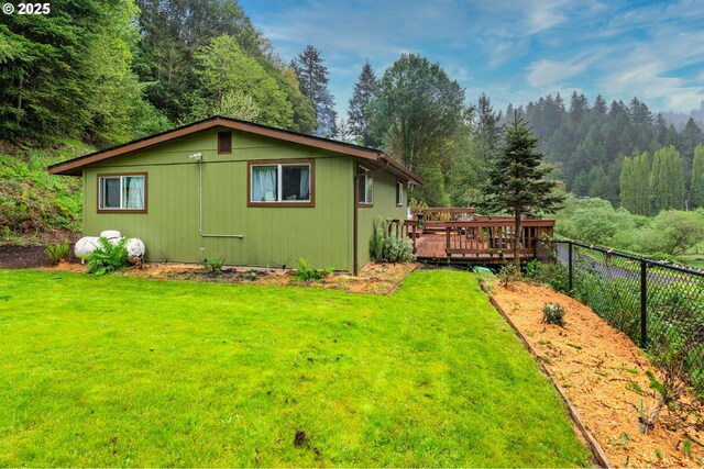 view of side of property with fence, a yard, a deck, and a forest view