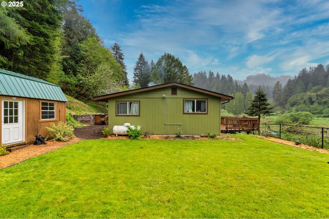 back of property featuring a lawn, a wooden deck, a view of trees, fence, and an outdoor structure