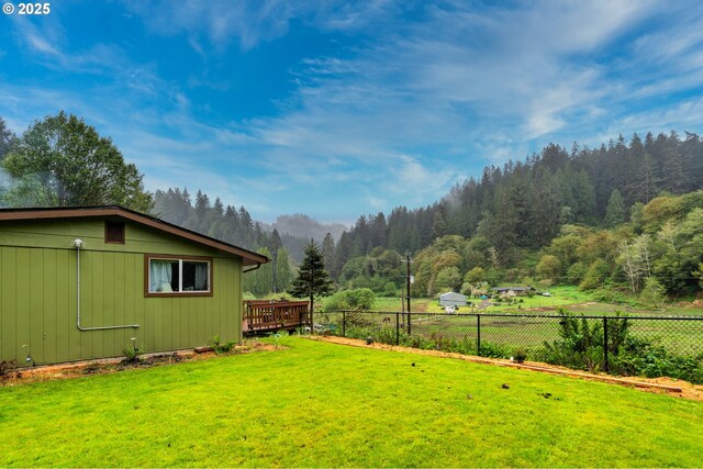 view of yard with a view of trees, fence, and a wooden deck
