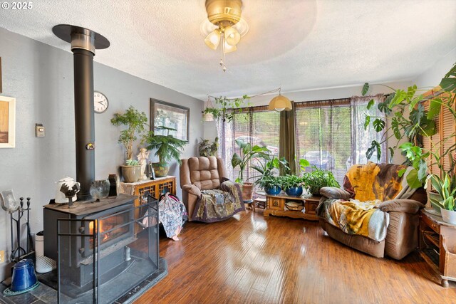 living area with a wood stove, a textured ceiling, a ceiling fan, and hardwood / wood-style floors