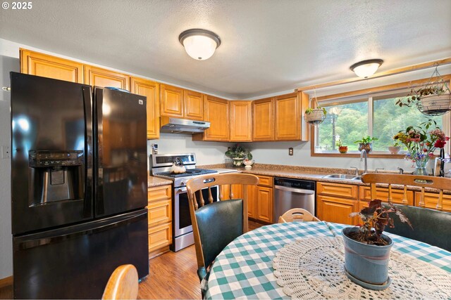 kitchen with under cabinet range hood, light countertops, appliances with stainless steel finishes, and light wood-type flooring
