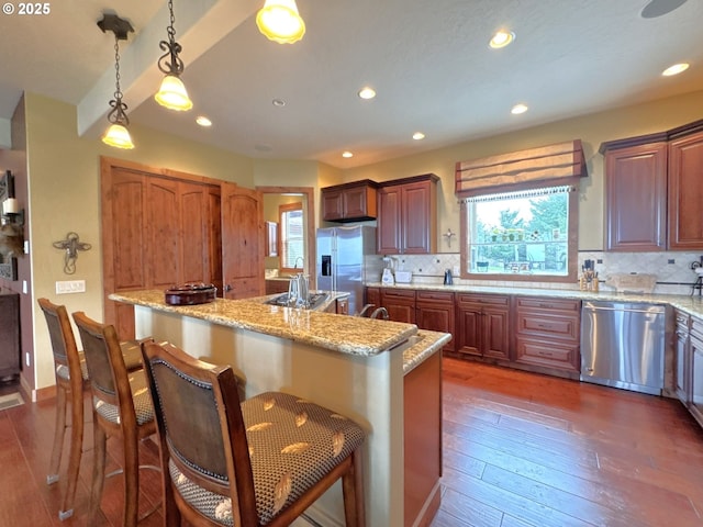kitchen with appliances with stainless steel finishes, decorative backsplash, a center island with sink, and a kitchen bar