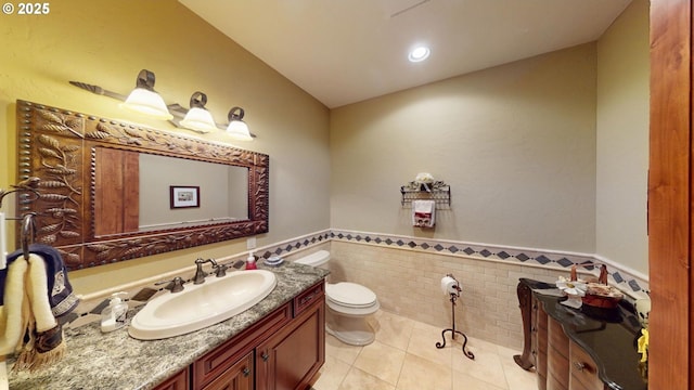 half bath featuring vanity, toilet, tile patterned floors, a wainscoted wall, and tile walls