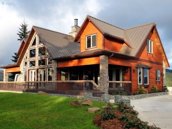 rear view of property with covered porch, stone siding, a chimney, metal roof, and a lawn