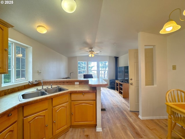 kitchen with a ceiling fan, a peninsula, lofted ceiling, light wood-style floors, and a sink