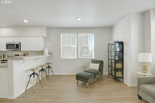 sitting room featuring light wood-type flooring, baseboards, a textured ceiling, and recessed lighting