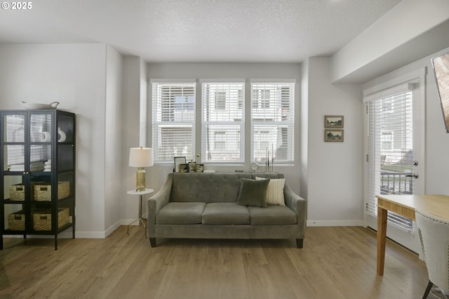 sitting room with light wood finished floors, baseboards, and a textured ceiling