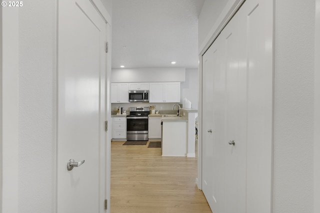 hall featuring light wood-style floors, recessed lighting, and a sink