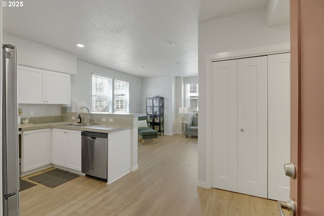 kitchen featuring appliances with stainless steel finishes, white cabinets, a sink, light wood-type flooring, and a peninsula