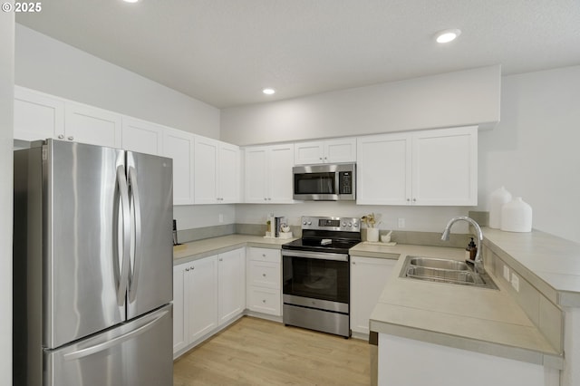 kitchen featuring stainless steel appliances, a peninsula, a sink, light wood-style floors, and light countertops