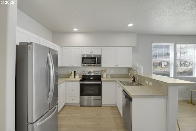 kitchen with appliances with stainless steel finishes, a peninsula, light countertops, light wood-style floors, and a sink