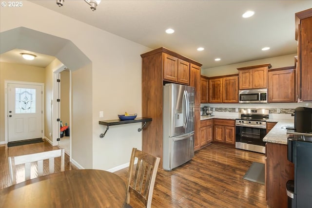 kitchen with dark wood-type flooring, recessed lighting, brown cabinets, appliances with stainless steel finishes, and arched walkways