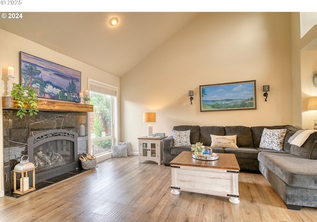 living room featuring high vaulted ceiling, a stone fireplace, and light hardwood / wood-style floors