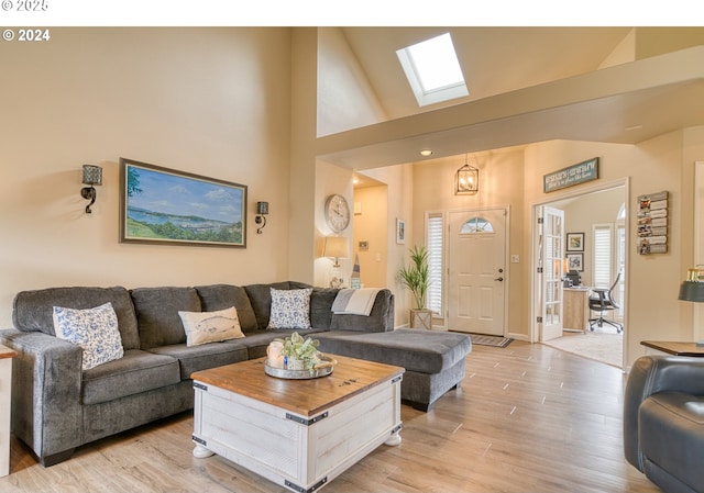 living room with light hardwood / wood-style floors, high vaulted ceiling, and a skylight