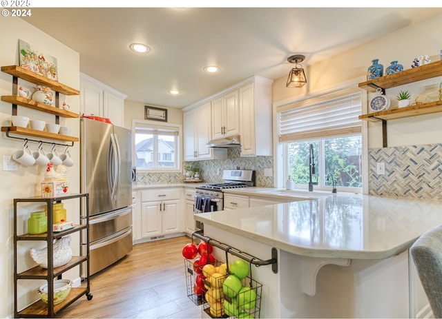 kitchen with appliances with stainless steel finishes, white cabinetry, decorative backsplash, kitchen peninsula, and light hardwood / wood-style flooring