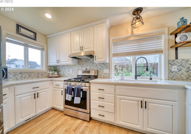 kitchen with light wood-type flooring, stainless steel gas stove, white cabinets, and sink