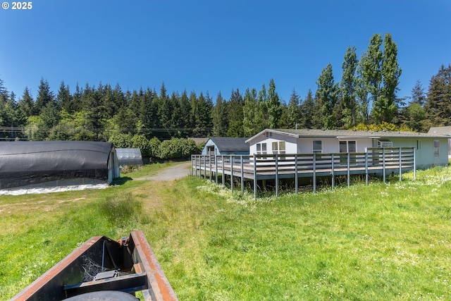 view of grassy yard with a view of trees and a deck