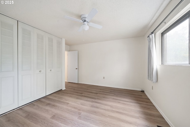 unfurnished bedroom with a closet, a ceiling fan, a textured ceiling, light wood-type flooring, and baseboards