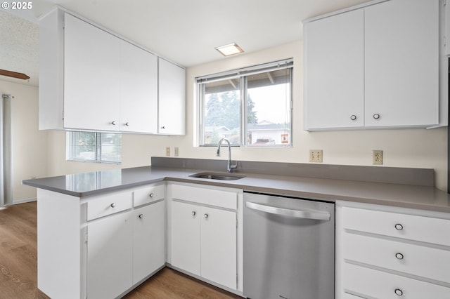 kitchen with a sink, a peninsula, white cabinets, and stainless steel dishwasher