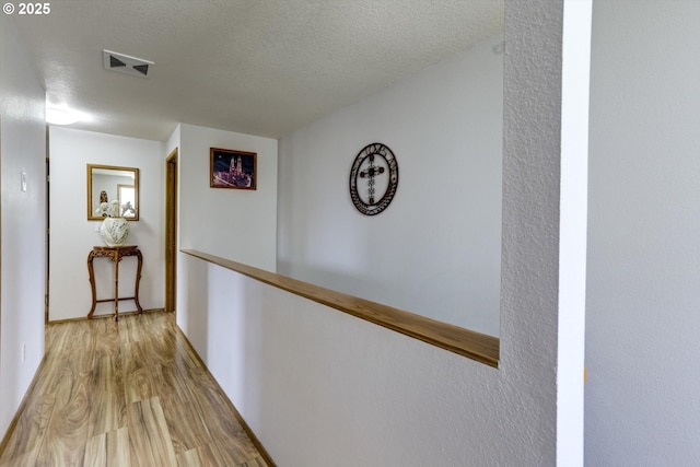 hallway featuring visible vents, wood finished floors, and a textured ceiling