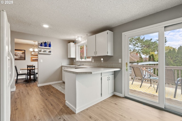 kitchen with white refrigerator with ice dispenser, light wood finished floors, light countertops, and a peninsula